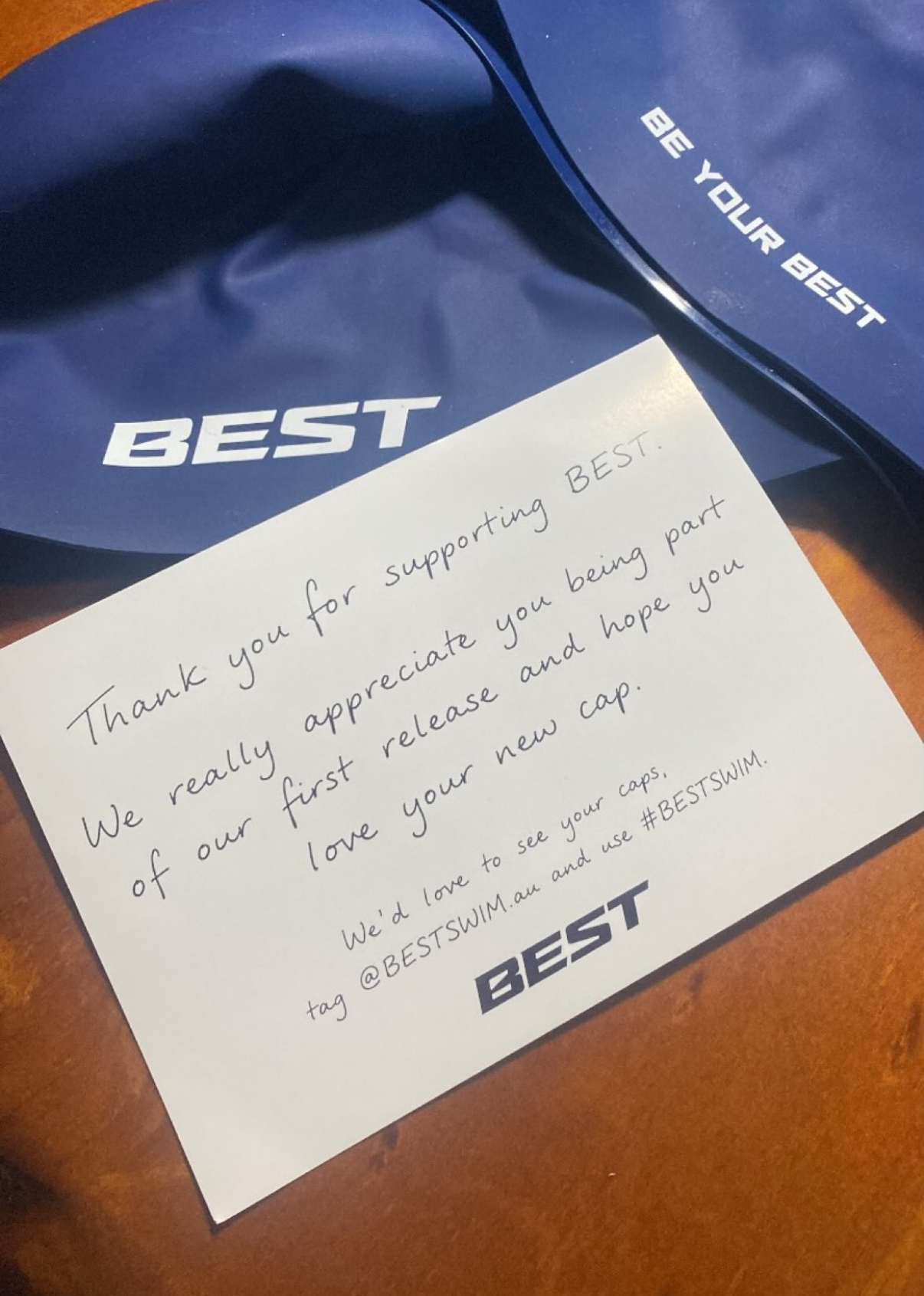Black, white and navy BEST caps hanging from a swim bag